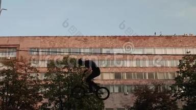 穿着黑色衣服的徒步旅行者跳上他的BMX自行车。 在背景上可以看到旧工业建筑。